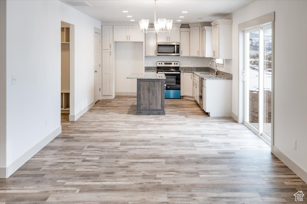 Kitchen with stainless steel appliances, light wood-type flooring, pendant lighting, and a center island