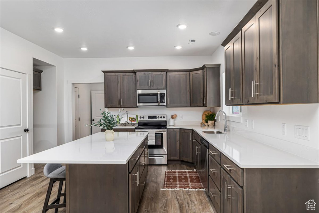 Kitchen with dark hardwood / wood-style flooring, a kitchen breakfast bar, appliances with stainless steel finishes, a center island, and sink
