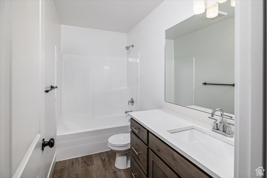 Full bathroom with vanity, toilet,  shower combination, and hardwood / wood-style floors
