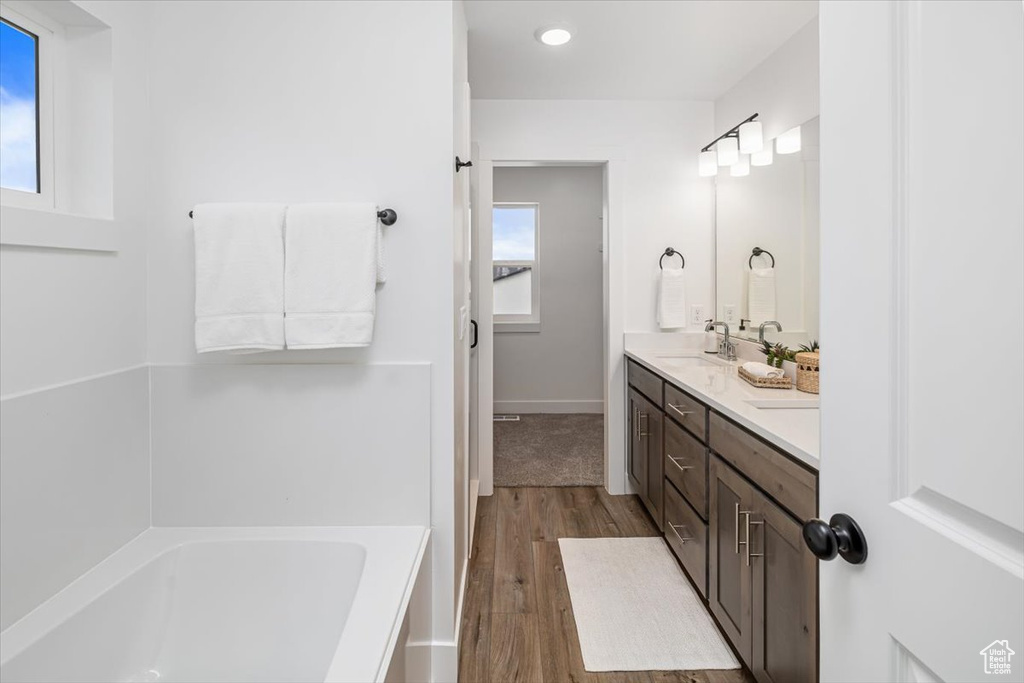 Bathroom with double vanity, plenty of natural light, a bathing tub, and hardwood / wood-style flooring
