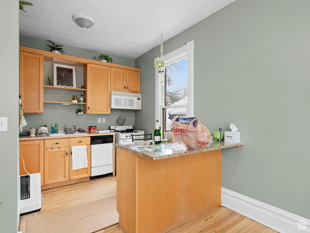 Kitchen with light stone countertops, light hardwood / wood-style floors, white appliances, and kitchen peninsula