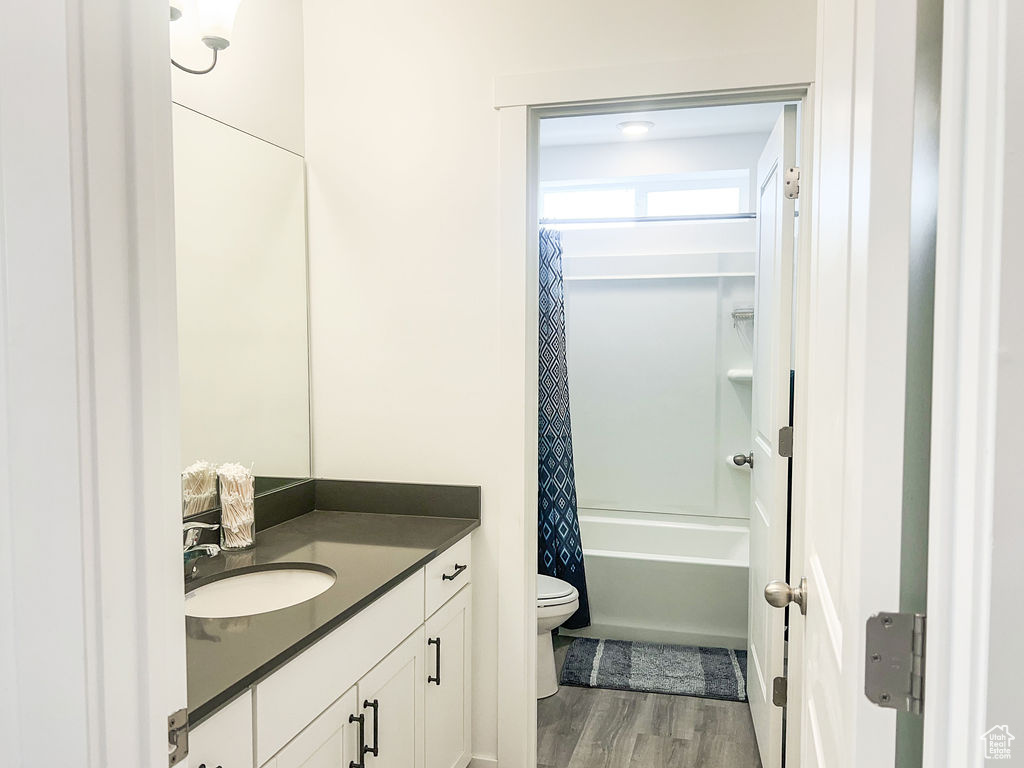 Full bathroom with toilet, large vanity, shower / bath combo, and hardwood / wood-style flooring