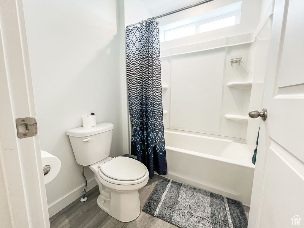 Bathroom featuring toilet, shower / bathtub combination with curtain, and hardwood / wood-style flooring