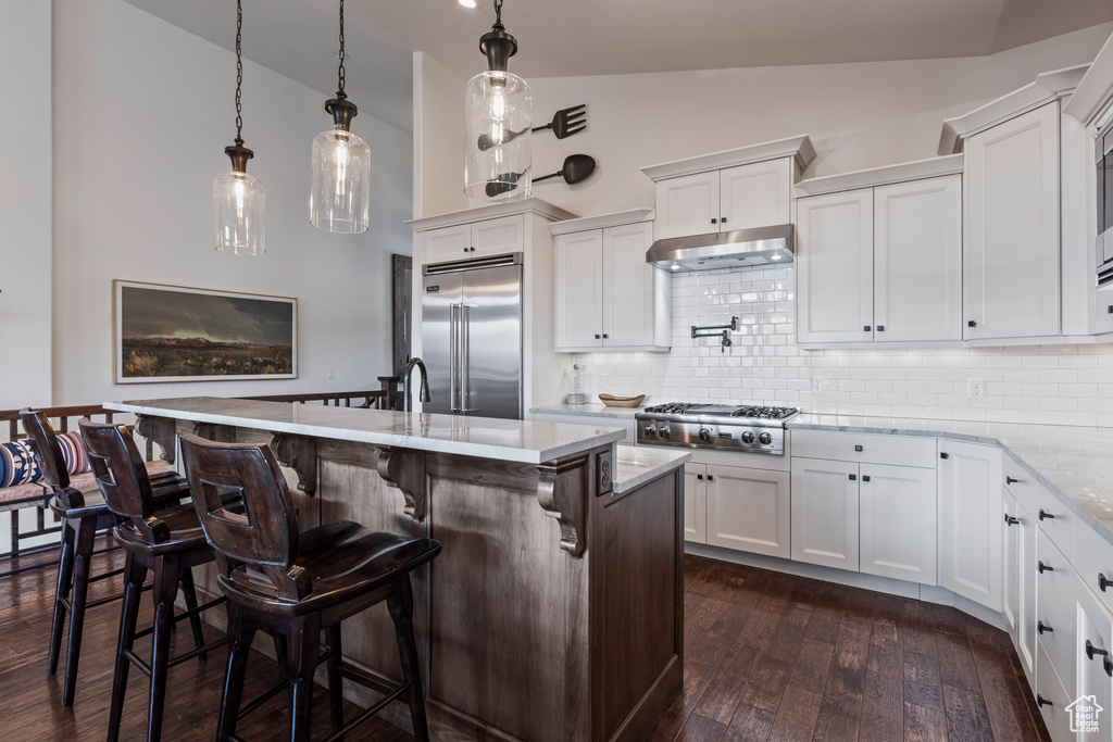 Kitchen featuring white cabinetry, vaulted ceiling, appliances with stainless steel finishes, decorative light fixtures, and dark hardwood / wood-style floors