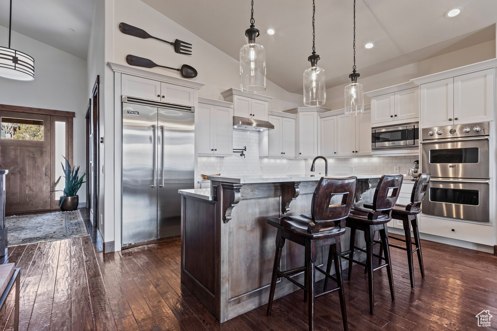 Kitchen with built in appliances, dark hardwood / wood-style flooring, a kitchen island with sink, and white cabinetry