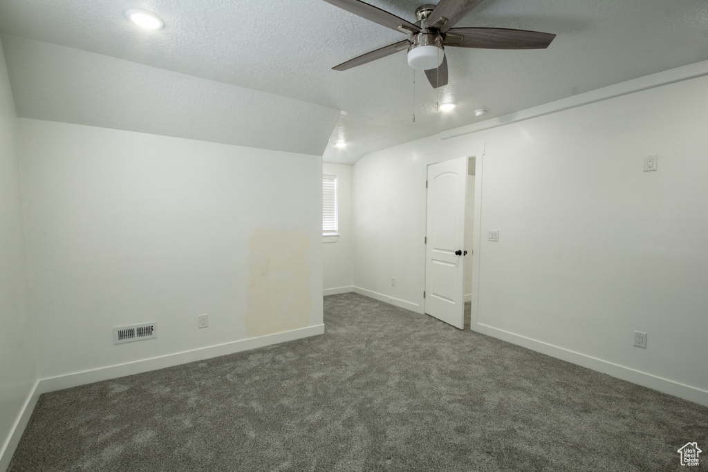 Spare room featuring vaulted ceiling, dark colored carpet, and ceiling fan