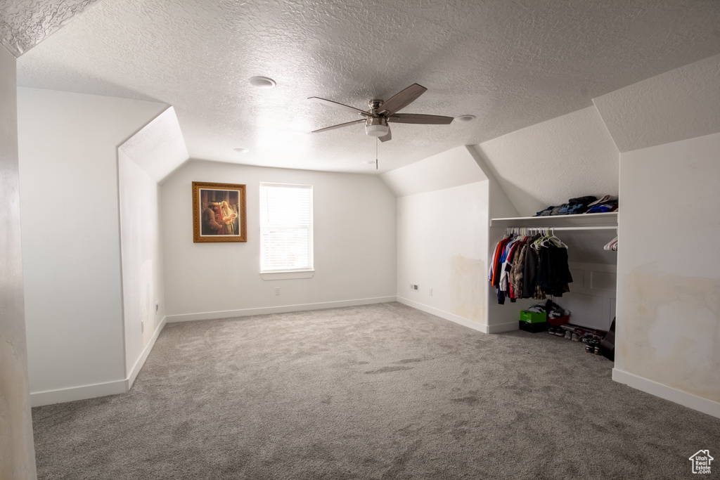Additional living space with lofted ceiling, light carpet, a textured ceiling, and ceiling fan