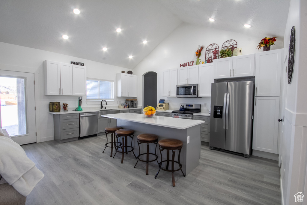 Kitchen with stainless steel appliances, light hardwood / wood-style floors, white cabinetry, a breakfast bar area, and a center island