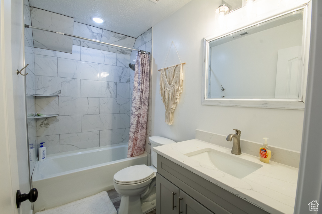 Full bathroom with toilet, vanity with extensive cabinet space, a textured ceiling, and shower / tub combo