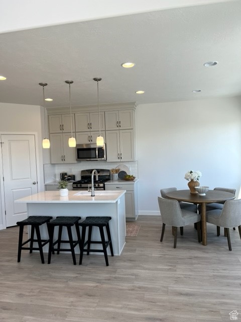 Kitchen with a kitchen breakfast bar, appliances with stainless steel finishes, tasteful backsplash, light hardwood / wood-style floors, and an island with sink