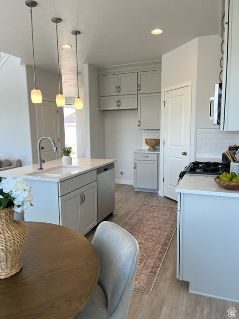 Kitchen with a kitchen island with sink, sink, tasteful backsplash, light hardwood / wood-style floors, and dishwasher