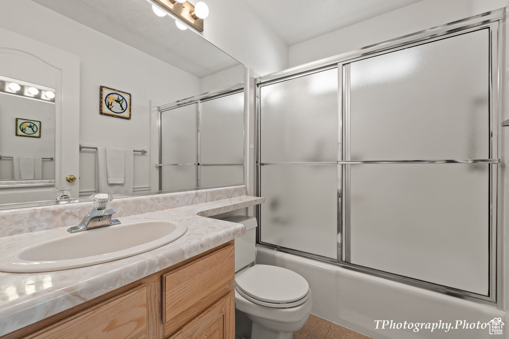 Full bathroom with bath / shower combo with glass door, vanity, toilet, and tile flooring