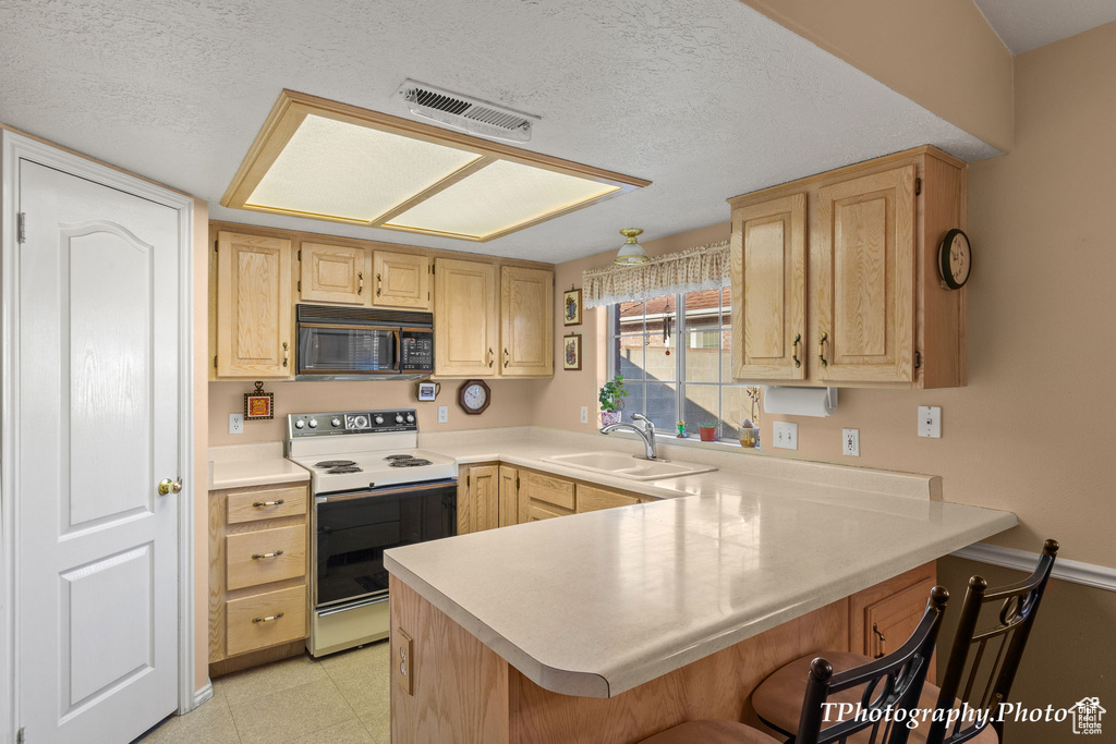 Kitchen with light brown cabinets, a breakfast bar, light tile floors, sink, and white electric range