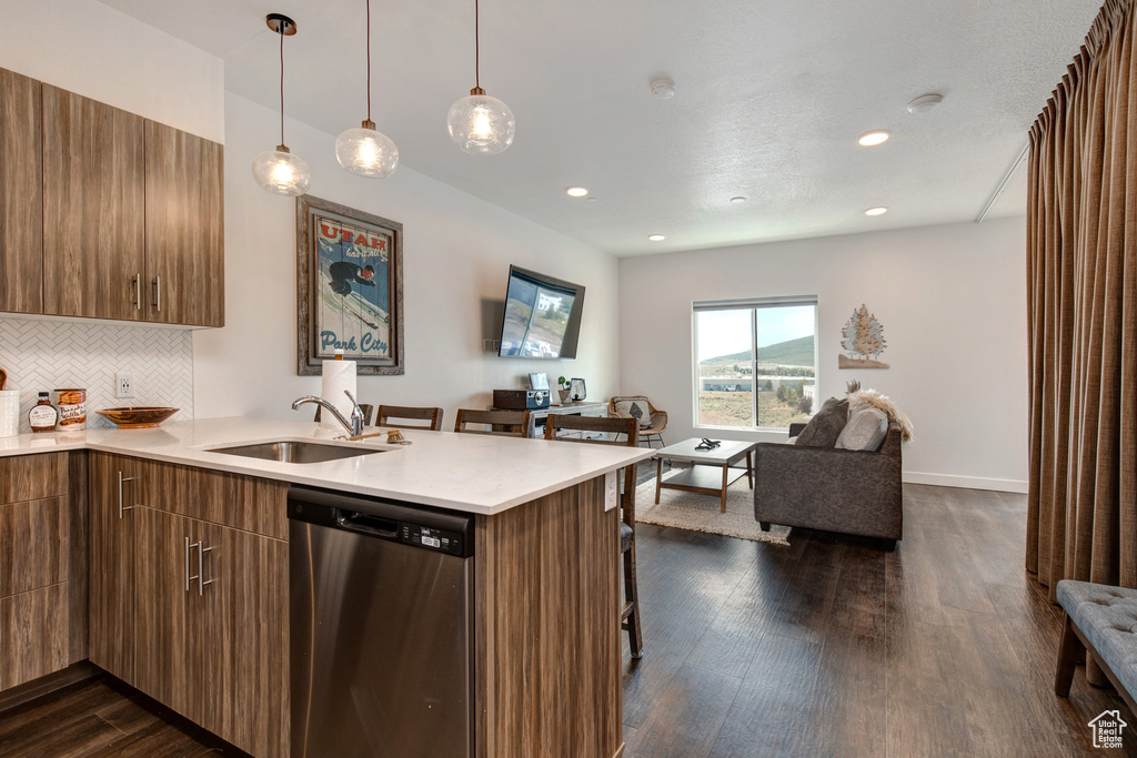 Kitchen with dark wood-type flooring, dishwasher, hanging light fixtures, and backsplash