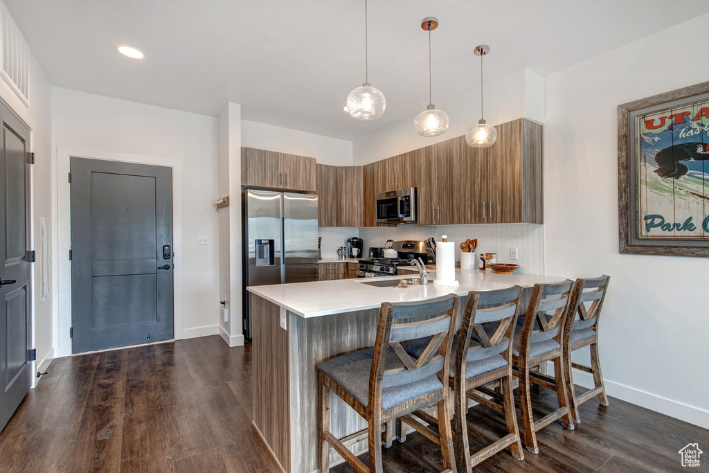 Kitchen featuring dark hardwood / wood-style flooring, a breakfast bar area, hanging light fixtures, kitchen peninsula, and stainless steel appliances