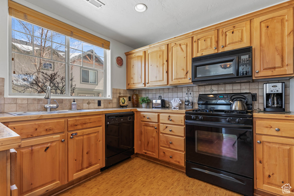 Kitchen with black appliances, light wood-type flooring, a wealth of natural light, backsplash, and sink