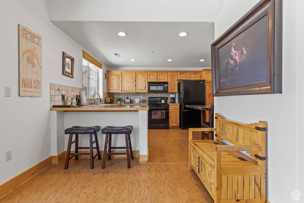 Kitchen with black appliances, a kitchen bar, kitchen peninsula, backsplash, and light hardwood / wood-style flooring