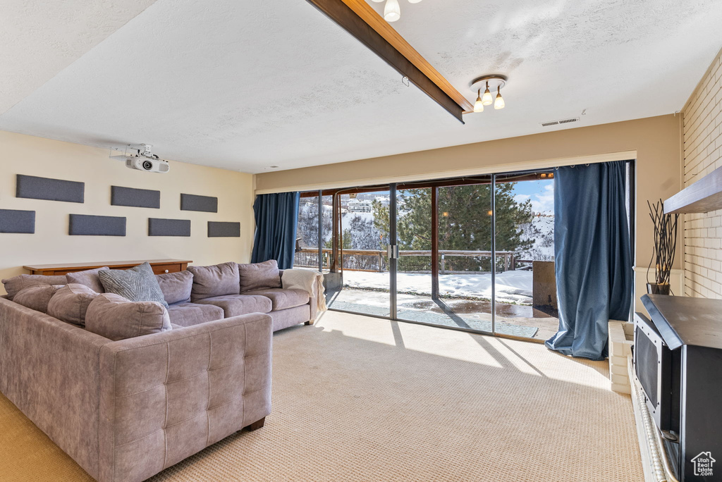 Carpeted living room featuring beam ceiling, a brick fireplace, and a textured ceiling