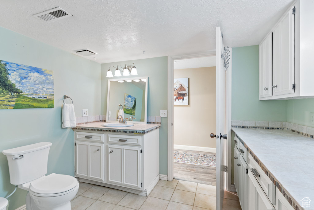 Bathroom featuring tile floors, toilet, vanity with extensive cabinet space, and a textured ceiling