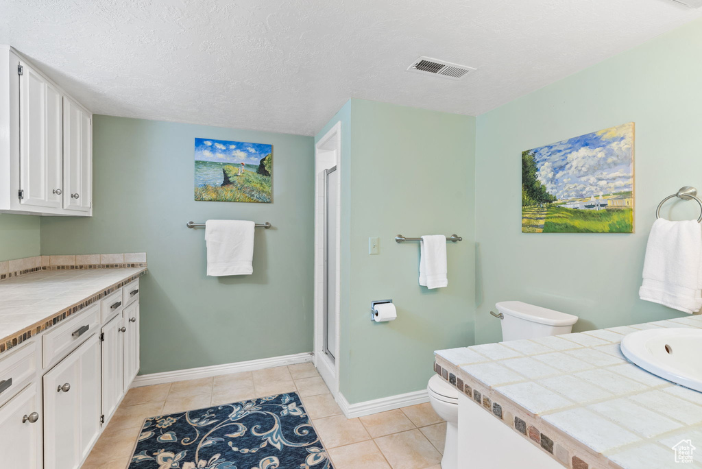Bathroom with toilet, vanity, tile flooring, an enclosed shower, and a textured ceiling