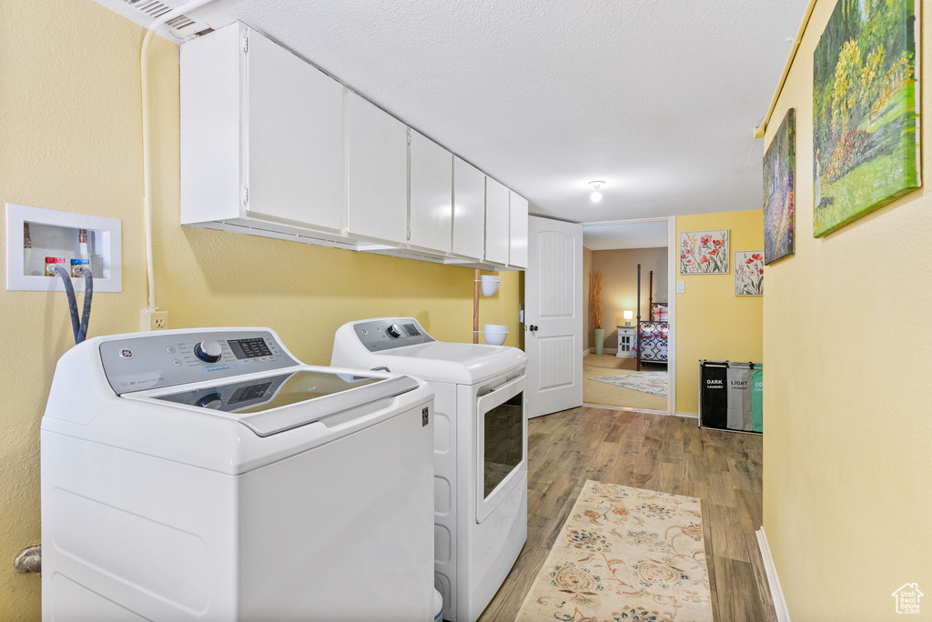 Laundry area with a textured ceiling, light hardwood / wood-style floors, washer and clothes dryer, and cabinets