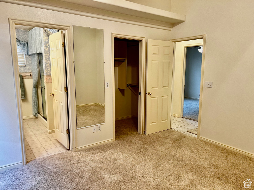 Unfurnished bedroom featuring a closet, ensuite bathroom, a walk in closet, and light carpet