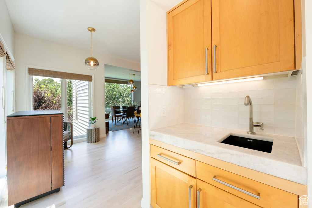 Kitchen with tasteful backsplash, sink, light wood-type flooring, and decorative light fixtures