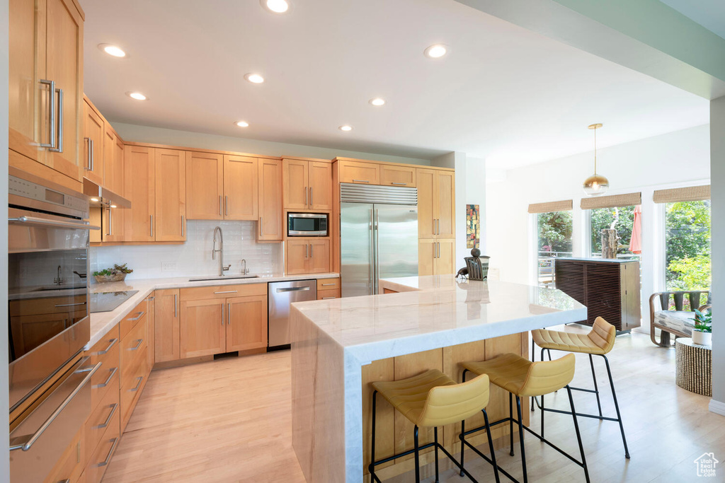 Kitchen featuring built in appliances, a breakfast bar, a kitchen island, backsplash, and light wood-type flooring