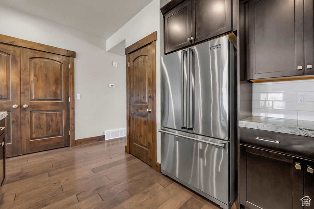 Kitchen with dark hardwood / wood-style floors, high quality fridge, dark brown cabinets, and backsplash
