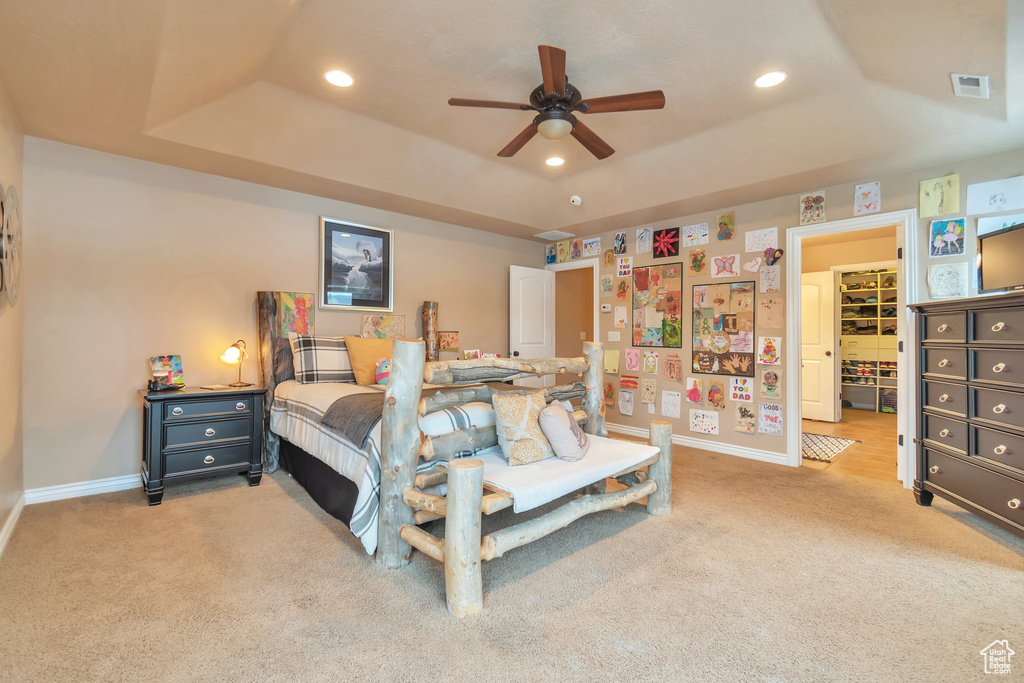 Carpeted bedroom featuring a tray ceiling, a closet, a walk in closet, and ceiling fan