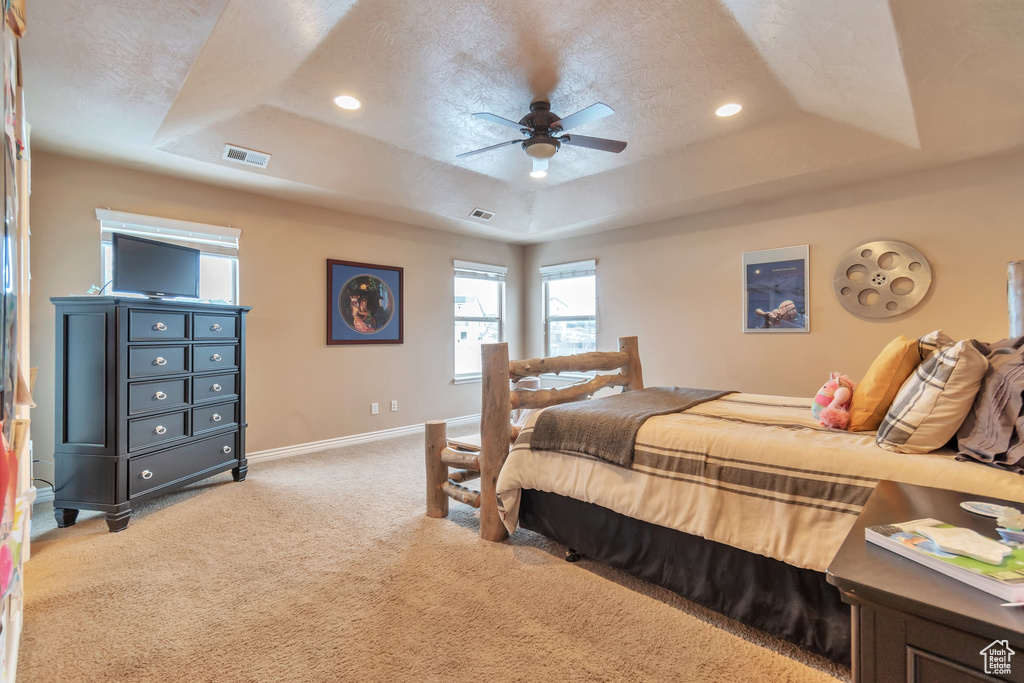 Carpeted bedroom featuring a textured ceiling, a tray ceiling, and ceiling fan