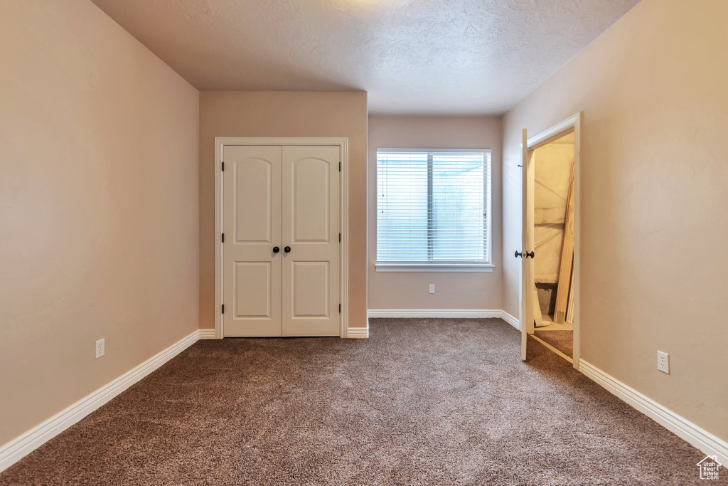 Unfurnished bedroom featuring a textured ceiling, a closet, and dark colored carpet
