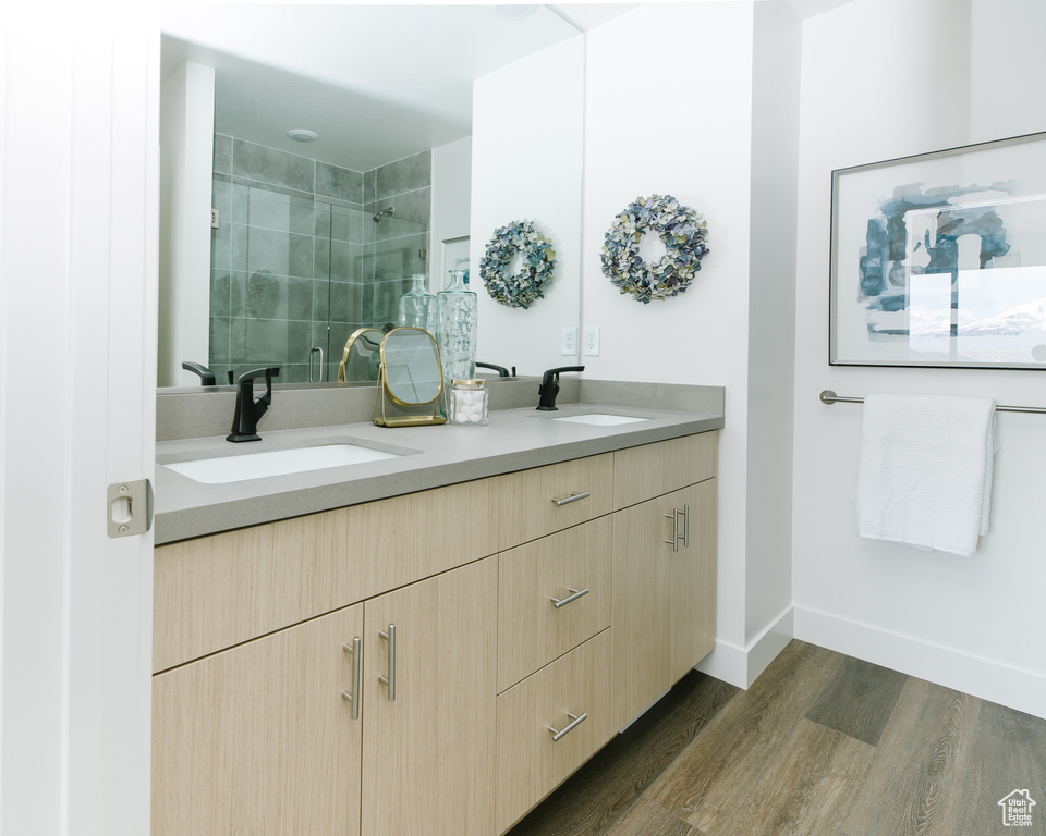 Bathroom featuring wood-type flooring, tiled shower, and dual bowl vanity