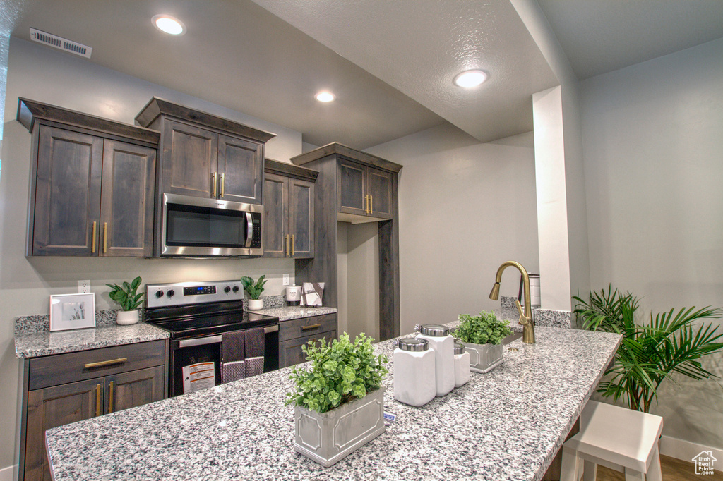 Kitchen featuring dark brown cabinets, a kitchen breakfast bar, light stone countertops, and stainless steel appliances
