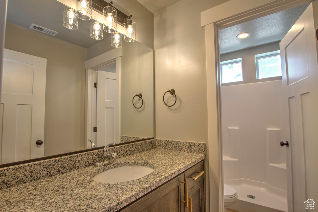 Bathroom with a notable chandelier, toilet, vanity, and walk in shower