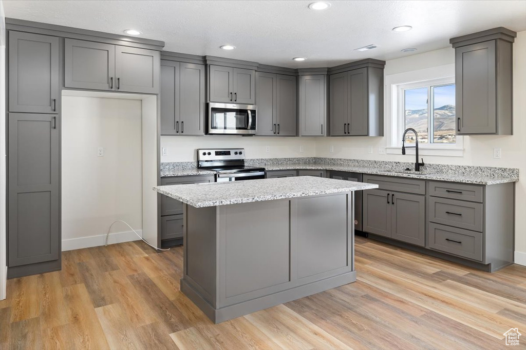 Kitchen featuring appliances with stainless steel finishes, a center island, gray cabinets, sink, and light wood-type flooring