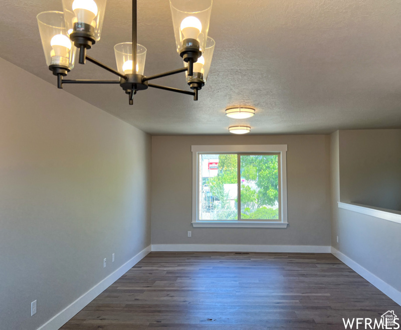 Empty room featuring an inviting chandelier, a textured ceiling, and dark wood-type flooring