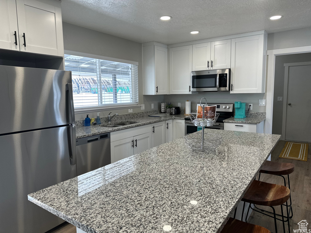 Kitchen featuring stainless steel appliances, white cabinets, a kitchen breakfast bar, and light stone counters