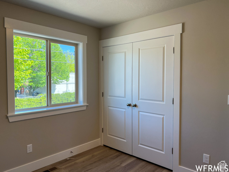 Unfurnished bedroom with dark hardwood / wood-style flooring, a closet, and multiple windows