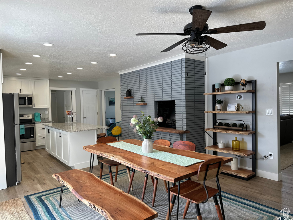 Dining room featuring a tile fireplace, light hardwood / wood-style floors, a textured ceiling, and ceiling fan