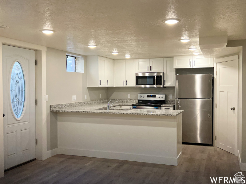 Kitchen with dark hardwood / wood-style floors, white cabinets, stainless steel appliances, and kitchen peninsula