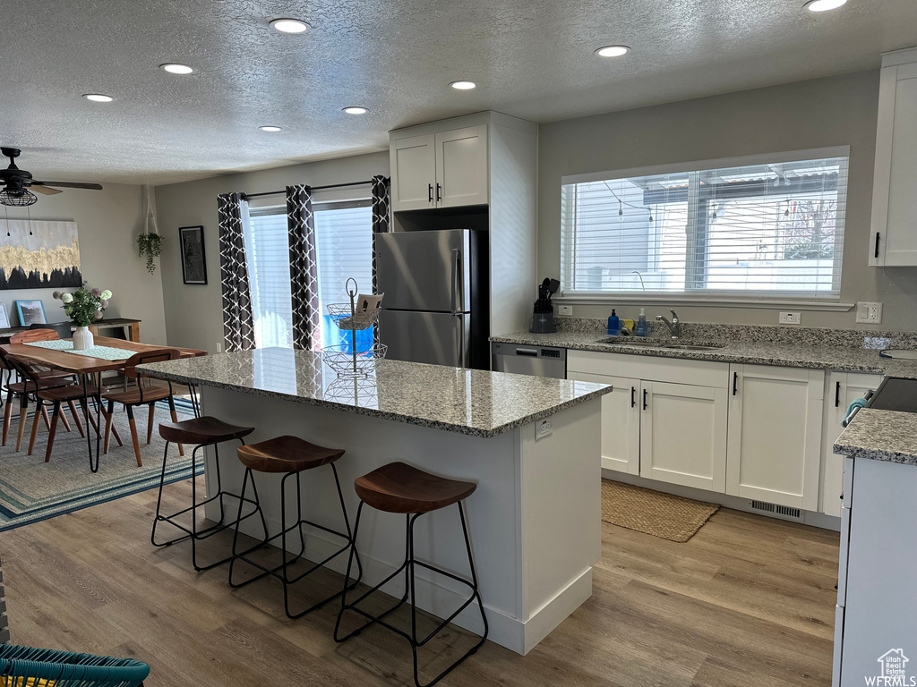 Kitchen with light hardwood / wood-style floors, ceiling fan, light stone counters, appliances with stainless steel finishes, and white cabinets