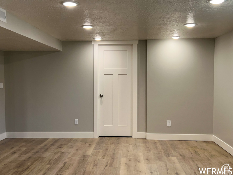 Basement featuring light wood-type flooring and a textured ceiling