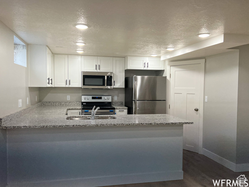 Kitchen with kitchen peninsula, dark hardwood / wood-style flooring, a textured ceiling, stainless steel appliances, and white cabinetry