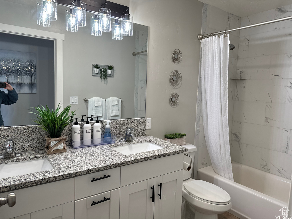 Full bathroom with oversized vanity, double sink, shower / bath combo with shower curtain, and toilet