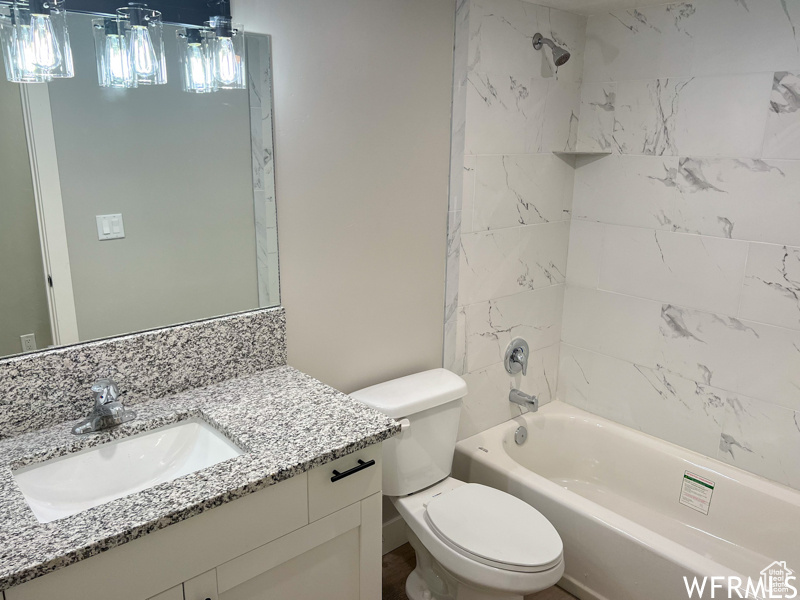 Full bathroom with tiled shower / bath combo, toilet, and large vanity