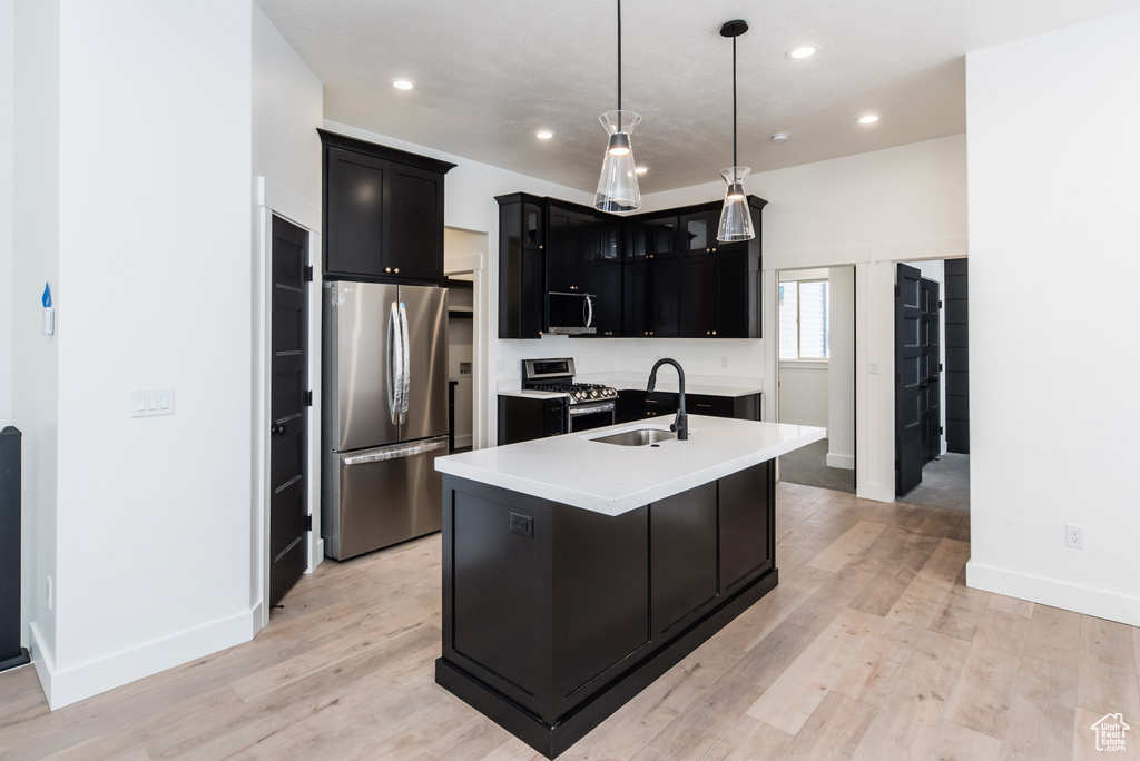 Kitchen featuring decorative light fixtures, appliances with stainless steel finishes, light hardwood / wood-style flooring, sink, and a center island with sink