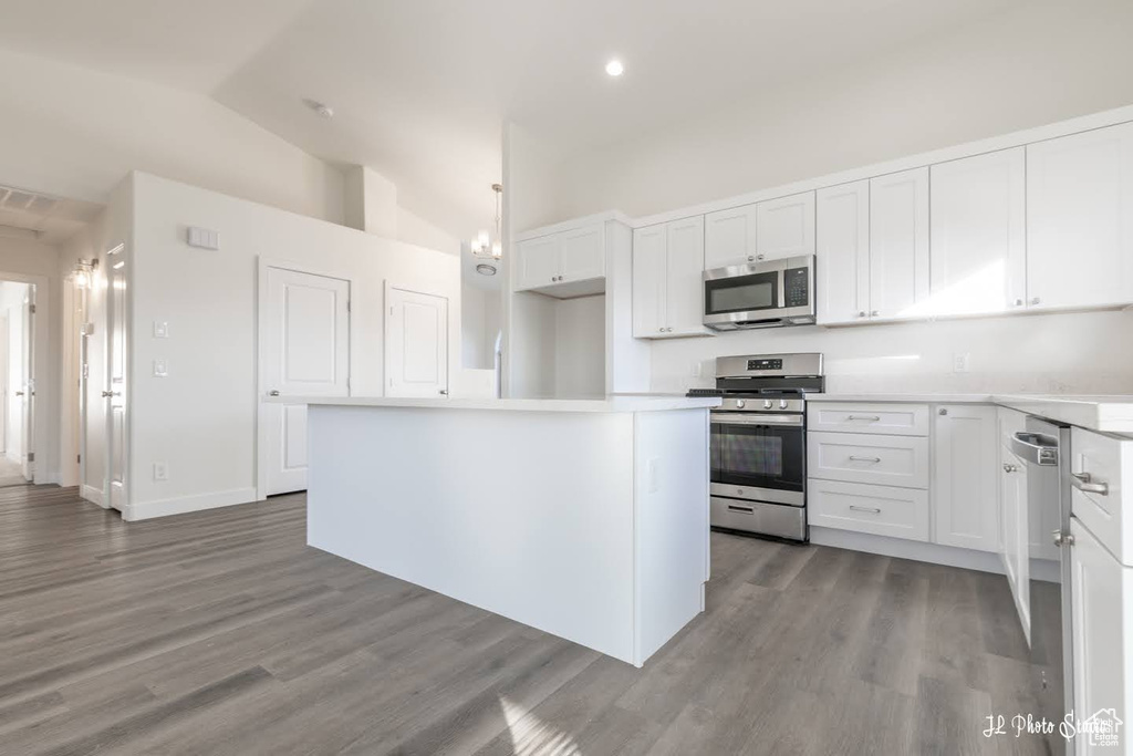 Kitchen with appliances with stainless steel finishes, a center island, light hardwood / wood-style flooring, vaulted ceiling, and white cabinetry