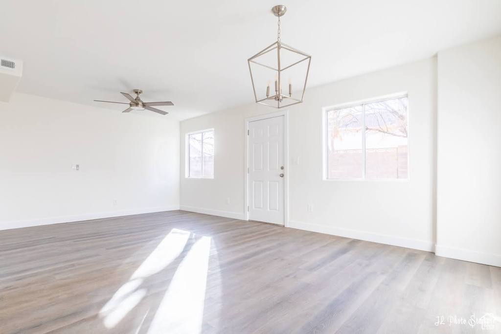 Spare room with ceiling fan with notable chandelier, a wealth of natural light, and light wood-type flooring