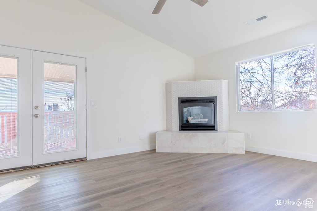 Unfurnished living room with a wealth of natural light, light wood-type flooring, a tiled fireplace, and ceiling fan